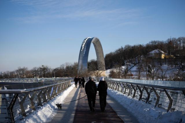 A couple walk their dog along the Klitschko Glass Bridge in Kyiv on February 17, 2026, amid the Russian invasion of Ukraine. (Photo by HENRY NICHOLLS / AFP)