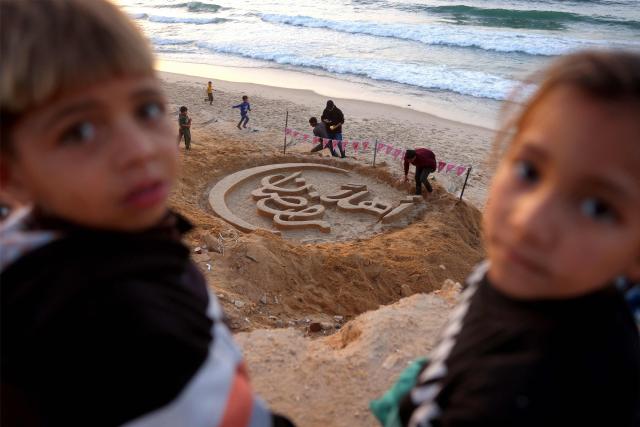 Children stand on a dune above a sand sculpture with the greeting message "Welcome, Ramadan" created by Palestinian artist Yazeed Abu Jarad, who was displaced by the war from Beit Lahia in the northern Gaza Strip, along a beach in Khan Yunis in the south of the Palestinian territory on February 17, 2026, a day ahead of the start of the Muslim holy month of Ramadan. (Photo by Bashar Taleb / AFP)