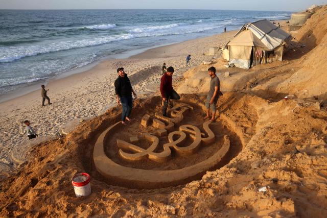 People assist Palestinian artist Yazeed Abu Jarad, who was displaced by the war from Beit Lahia in the northern Gaza Strip, as he creates a sand sculpture with the greeting message "Welcome, Ramadan" along a beach in Khan Yunis in the south of the Palestinian territory on February 17, 2026, a day ahead of the start of the Muslim holy month of Ramadan. (Photo by Bashar Taleb / AFP)