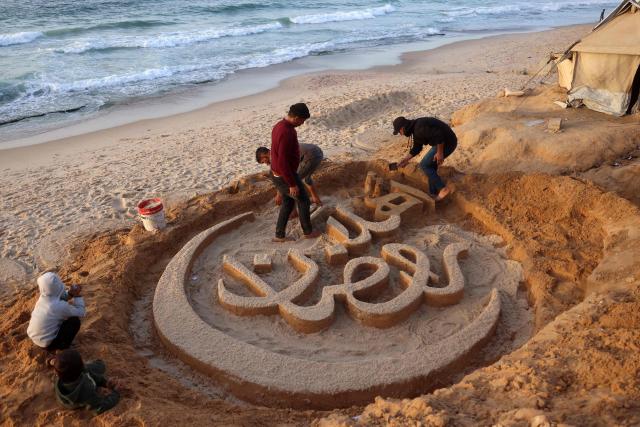 TOPSHOT - People assist Palestinian artist Yazeed Abu Jarad, who was displaced by the war from Beit Lahia in the northern Gaza Strip, as he creates a sand sculpture with the greeting message "Welcome, Ramadan" along a beach in Khan Yunis in the south of the Palestinian territory on February 17, 2026, a day ahead of the start of the Muslim holy month of Ramadan. (Photo by Bashar Taleb / AFP)