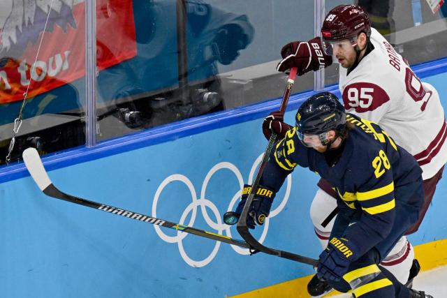 Sweden's #28 Elias Lindholm (L) vies for the puck with Latvia's #95 Oskars Batna during the men's qualification play-off ice hockey match between Sweden and Latvia at the Milano Santagiulia Ice Hockey Arena during the Milano Cortina 2026 Winter Olympic Games in Milan, on February 17, 2026. (Photo by Alexander NEMENOV / AFP)