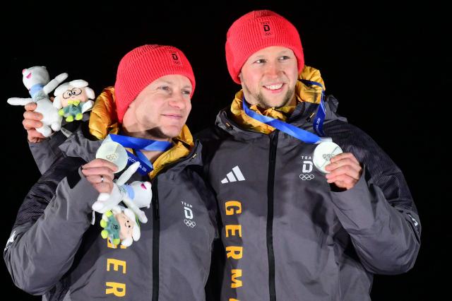 Silver medallists Germany's Francesco Friedrich and Germany's Alexander Schueller, celebrate on the podium after competing in the bobsleigh men's 2-man event at Cortina Sliding Centre during the Milano Cortina 2026 Winter Olympic Games in Cortina d'Ampezzo on February 17, 2026. (Photo by Stefano RELLANDINI / AFP)