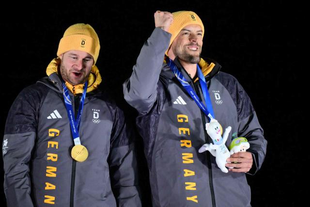 Gold medallists Germany's Johannes Lochner (L) and Germany's Georg Fleischhauer celebrate on the podium after competing in the bobsleigh men's 2-man event at Cortina Sliding Centre during the Milano Cortina 2026 Winter Olympic Games in Cortina d'Ampezzo on February 17, 2026. (Photo by Stefano RELLANDINI / AFP)