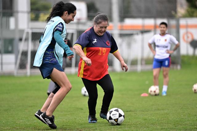 Retired teacher Angelica Aguirre, 73, vies for the ball with Camila Sanchez during a training session within the Women’s Football Comprehensive Training Programme at the Catholic University in Quito on February 4, 2026. The Centre for Knowledge Transfer and Social Innovation at the Catholic University of Quito fosters a safe and inclusive space in which women can participate in the football team, regardless of their age. (Photo by Rodrigo BUENDIA / AFP)