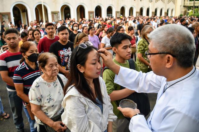 A seminarian applies ash to the foreheads of Catholic devotees on Ash Wednesday at a church ground in Manila on February 18, 2026. (Photo by Ted ALJIBE / AFP)