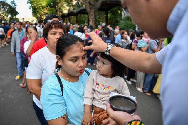 A seminarian applies ash to the foreheads of Catholic devotees on Ash Wednesday at a church ground in Manila on February 18, 2026. (Photo by Ted ALJIBE / AFP)