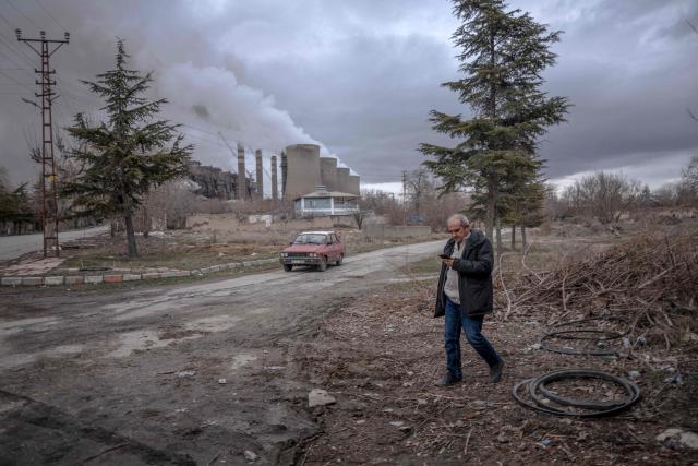 Mehmet Dalkanat, spokesman of local platform to protect life and nature, walks on a street as clouds of water vapor rise from the Afsin-Elbistan coal-based power plant in the nearby village of Cogulhan on February 11, 2026. The power plant has operated since 1984 and is one of Turkey's largest thermal facilities, with eight units generating 2,795 megawatts. It relies on lignite from the Afsin?Elbistan basin, which holds around 40 percent of the country's known reserves. Environmental groups say they are alarmed by government plans to expand Plant A with two new units as part of efforts to reduce reliance on energy imports. (Photo by Ozan KOSE / AFP)