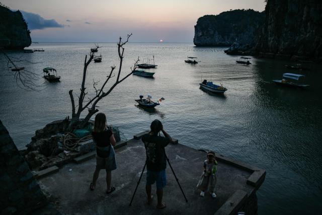 A photographer (C) takes photo of the sunset on Vietnam's Cat Ba island on February 16, 2026. (Photo by Amaury PAUL / AFP)