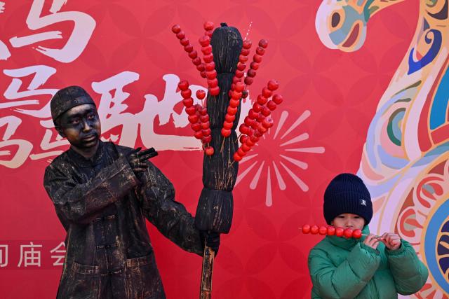 A boy (R) stands next to a man dressed in a statue-ispired outfits (L) during a temple fair on the second day of the Lunar New Year of the Horse in Beijing on February 18, 2026. (Photo by Adek BERRY / AFP)