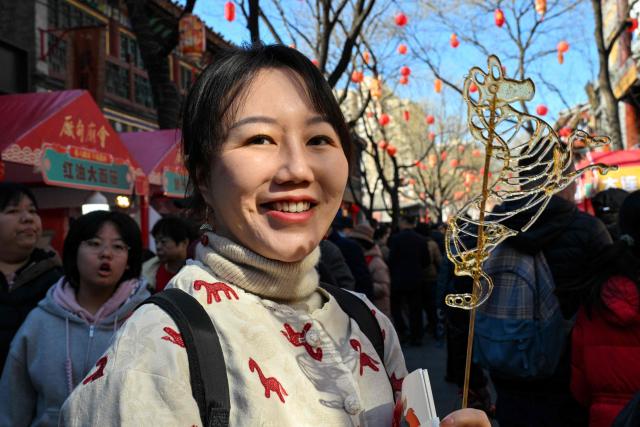A woman (C) holds a horse-shaped candy as people visit a temple fair on the second day of the Lunar New Year of the Horse in Beijing on February 18, 2026. (Photo by Adek BERRY / AFP)
