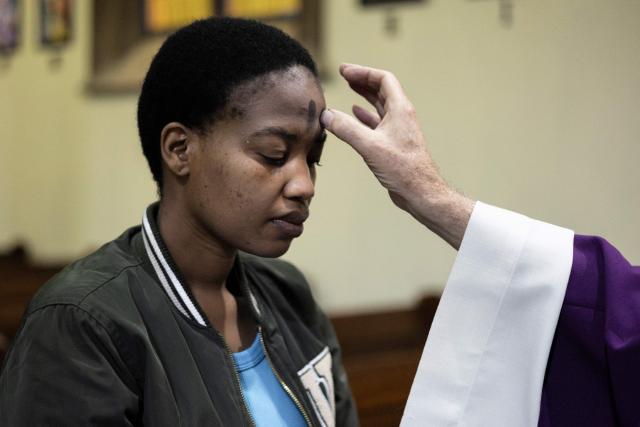 The parish priest marks a cross with ashes on a Catholic's forehead during the Ash Wednesday Mass at the Holy Trinity Catholic Church in Braamfontein, Johannesburg, on February 18, 2026. (Photo by ILARIA FINIZIO / AFP)