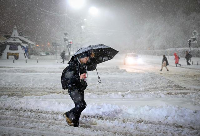 A man walks on a boulevard under heavy snowfall in Bucharest, Romania, on February 18, 2026. Romanian authorities issued a Code Orange warning for several counties, as heavy snowfall and blizzard conditions disrupted transport and forced schools to close across the country's southern and eastern regions. (Photo by Daniel MIHAILESCU / AFP)