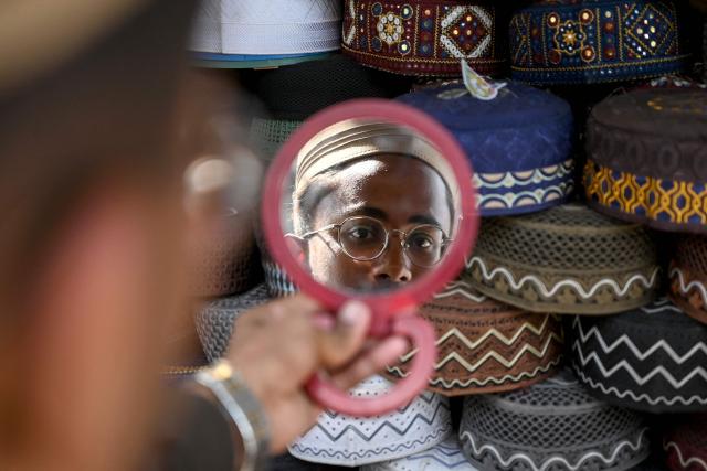 A man tries a traditional prayer cap at a roadside shop ahead of the Islamic holy fasting month of Ramadan in Karachi on February 18, 2026. (Photo by Rizwan TABASSUM / AFP)