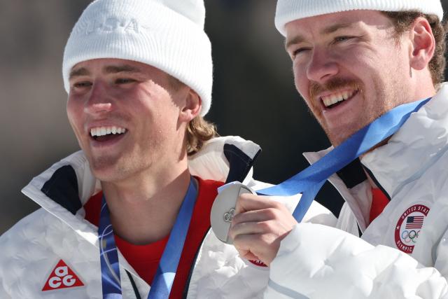 (From L) Silver medallists USA's Gus Schumacher and USA's Ben Ogden celebrate on the podium of the men's team cross country free sprint final event of the Milano Cortina 2026 Winter Olympic Games at Tesero Cross-Country Skiing Stadium in Lago di Tesero (Val di Fiemme), on February 18, 2026. (Photo by Anne-Christine POUJOULAT / AFP)