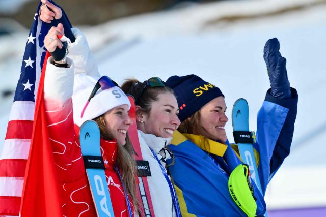 From (L-R) Switzerland's silver medalist Camille Rast, USA's gold medalist Mikaela Shiffrin, and  Sweden's bronze medalist Anna Swenn Larsson celebrate on the podium of the women's slalom event during the Milano Cortina 2026 Winter Olympic Games at the Tofane Alpine Skiing Centre in Cortina d’Ampezzo on February 18, 2026. (Photo by Stefano RELLANDINI / AFP)