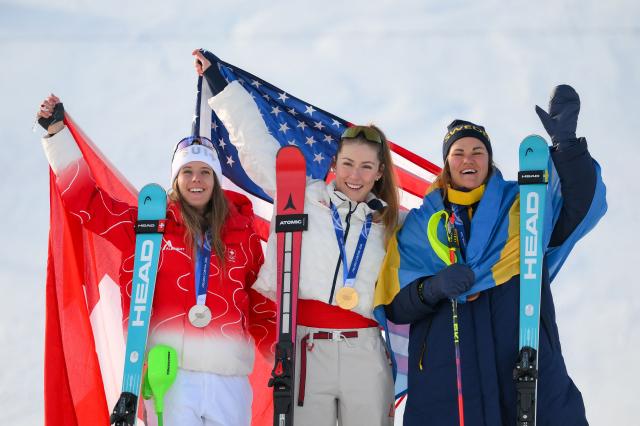 (From L) Switzerland's silver medalist Camille Rast, USA's gold medalist Mikaela Shiffrin, and Sweden's bronze medalist Anna Swenn Larsson celebrate on the podium of the women's slalom event during the Milano Cortina 2026 Winter Olympic Games at the Tofane Alpine Skiing Centre in Cortina d’Ampezzo on February 18, 2026. (Photo by Marco BERTORELLO / AFP)
