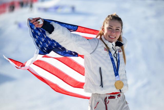 USA's gold medalist Mikaela Shiffrin celebrates with her national flag during the podium ceremony of the women's slalom event during the Milano Cortina 2026 Winter Olympic Games at the Tofane Alpine Skiing Centre in Cortina d’Ampezzo on February 18, 2026. (Photo by Marco BERTORELLO / AFP)