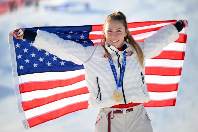 USA's gold medalist Mikaela Shiffrin celebrates with her national flag during the podium ceremony of the women's slalom event during the Milano Cortina 2026 Winter Olympic Games at the Tofane Alpine Skiing Centre in Cortina d’Ampezzo on February 18, 2026. (Photo by Marco BERTORELLO / AFP)