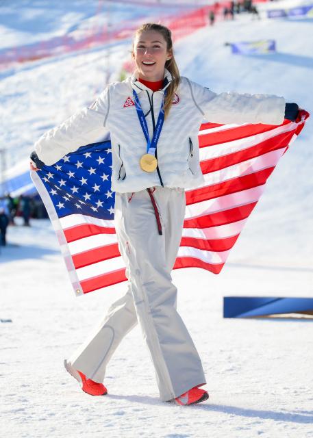Gold medallist USA's Mikaela Shiffrin celebrates with the national flag after the women's slalom event during the Milano Cortina 2026 Winter Olympic Games at the Tofane Alpine Skiing Centre in Cortina d’Ampezzo on February 18, 2026. (Photo by Marco BERTORELLO / AFP)