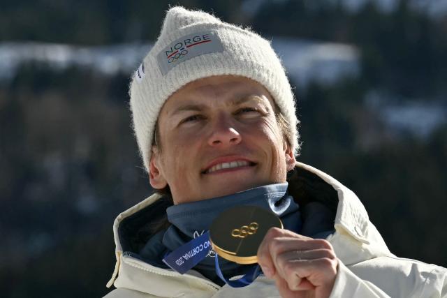 Gold medallist Norway's Johannes Hoesflot Klaebo celebrates on the podium for the men's team cross country free sprint final event of the Milano Cortina 2026 Winter Olympic Games at Tesero Cross-Country Skiing Stadium in Lago di Tesero (Val di Fiemme), on February 18, 2026. (Photo by Javier SORIANO / AFP)