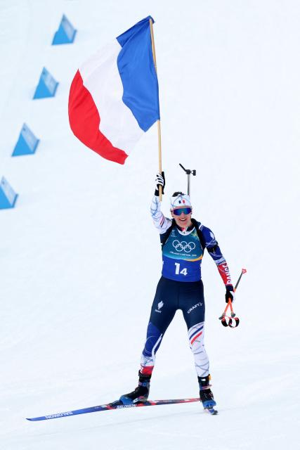 France's Julia Simon approaches the finish line while holding a French flag to win gold in the women's biathlon 4x6km relay event during the Milano Cortina 2026 Winter Olympic Games at the Anterselva Biathlon Arena (Sudtirol Arena) in Anterselva (Val Pusteria) on February 18, 2026. (Photo by Odd ANDERSEN / AFP)