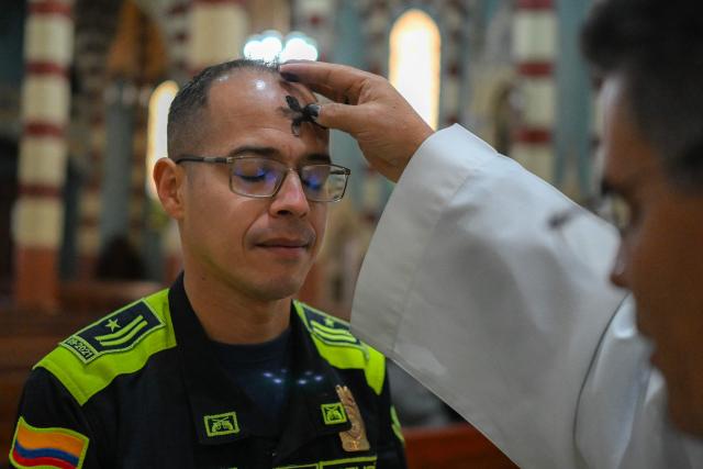 A Colombian policeman receives the sign of the cross in ashes on his forehead from a priest during Ash Wednesday celebrations at Santuario El Carmen in Bogota on February 18, 2026. Ash Wednesday marks the Christian period of Lent, prior to the Holy Week. (Photo by Luis ACOSTA / AFP)