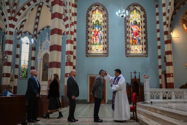 People wait in line to receive the sign of the cross in ashes on their foreheads from a priest during Ash Wednesday celebrations at Santuario El Carmen in Bogota on February 18, 2026. Ash Wednesday marks the Christian period of Lent, prior to the Holy Week. (Photo by Luis ACOSTA / AFP)