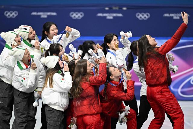 Team South Korea, team Italy and team Canada pose for a selfie at the podium of  the short track speed skating women's 3000m relay final during the Milano Cortina 2026 Winter Olympic Games at Milano Ice Skating Arena in Milan on February 18, 2026. (Photo by Gabriel BOUYS / AFP)