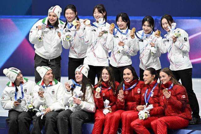 Team South Korea, team Italy and team Canada pose for pictures at the podium of  the short track speed skating women's 3000m relay final during the Milano Cortina 2026 Winter Olympic Games at Milano Ice Skating Arena in Milan on February 18, 2026. (Photo by Gabriel BOUYS / AFP)