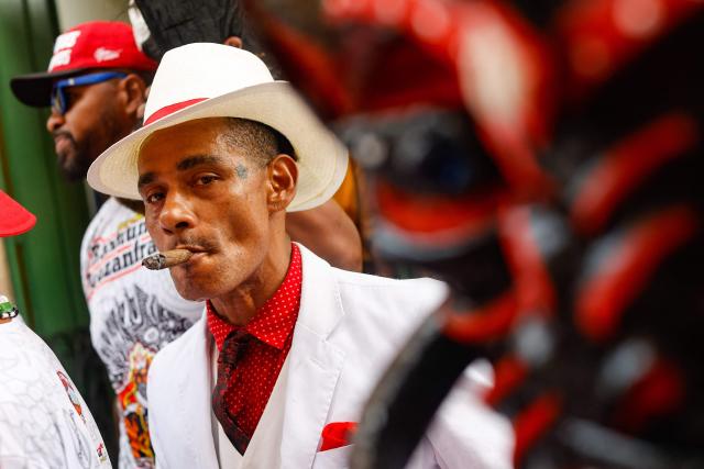 A reveller smokes during the Raimundo Bouzanfraim procession in the Pelourinho district of Salvador, Bahia state, Brazil, on February 18, 2026, marking the beginning of Ash Wednesday and celebrating Afro-Brazilian spirituality and ancestry. This year, the parade celebrates ancestry and Afro-Brazilian spirituality, with the theme of Exu as a symbol of movement, renewal and the connection between past, present and future. (Photo by Rafael Martins / AFP)