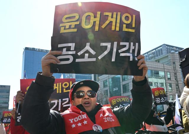 Supporters of South Korea's impeached former president Yoon Suk Yeol hold up placards reading "Yoon again!" as they gather in front of the Seoul Central District Court in Seoul on February 19, 2026. A South Korean court will rule on February 19, on insurrection charges against ex-president Yoon Suk Yeol, weighing whether he should be sentenced to death for his failed bid to impose military rule. (Photo by Jung Yeon-je / AFP)