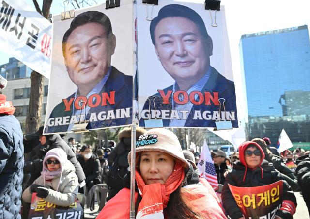 A supporter of South Korea's impeached former president Yoon Suk Yeol holds a placard showing a photo of Yoon as they gather in front of the Seoul Central District Court in Seoul on February 19, 2026. A South Korean court will rule on February 19, on insurrection charges against ex-president Yoon Suk Yeol, weighing whether he should be sentenced to death for his failed bid to impose military rule. (Photo by Jung Yeon-je / AFP)