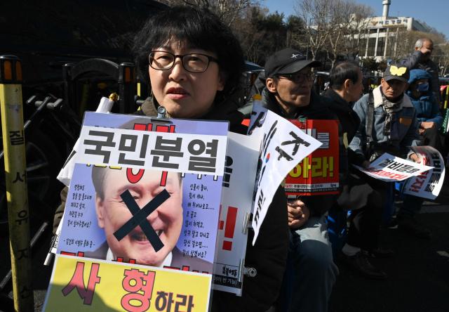 A protester holds a placard showing a photo of South Korea's impeached former president Yoon Suk Yeol with words reading "A death sentence" during a rally against Yoon near the Seoul Central District Court in Seoul on February 19, 2026. A South Korean court will rule on February 19, on insurrection charges against ex-president Yoon Suk Yeol, weighing whether he should be sentenced to death for his failed bid to impose military rule. (Photo by Jung Yeon-je / AFP)