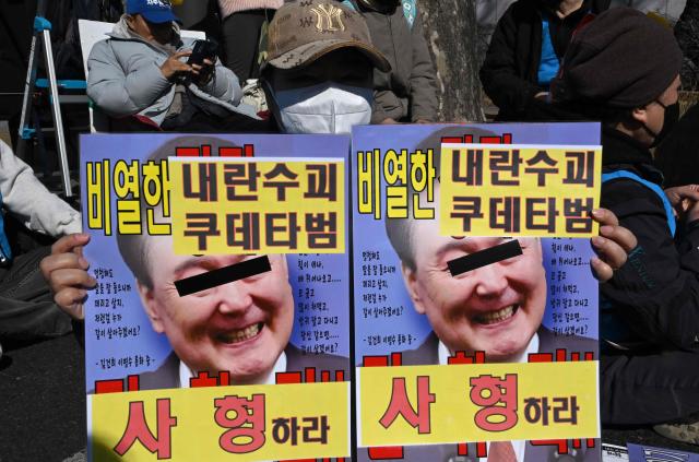 A protester holds a placard showing a photo of South Korea's impeached former president Yoon Suk Yeol with words reading "A death sentence" during a rally against Yoon near the Seoul Central District Court in Seoul on February 19, 2026. A South Korean court will rule on February 19, on insurrection charges against ex-president Yoon Suk Yeol, weighing whether he should be sentenced to death for his failed bid to impose military rule. (Photo by Jung Yeon-je / AFP)