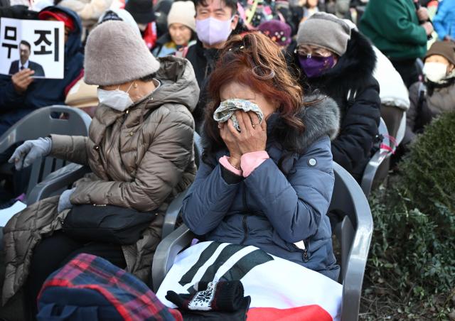 Supporters of South Korea's impeached former president Yoon Suk Yeol react as they watch a live stream of Yoon's trial on his insurrection charges near the Seoul Central District Court in Seoul on February 19, 2026. A South Korean court found ex-president Yoon Suk Yeol guilty of insurrection on February 19, and sentenced him to life in prison, saying his martial law declaration in December 2024 was a plot to "paralyse" the National Assembly. (Photo by Jung Yeon-je / AFP)