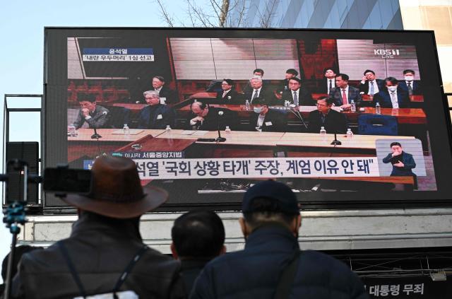 Supporters of South Korea's impeached former president Yoon Suk Yeol watch a live stream of Yoon's trial on his insurrection charges near the Seoul Central District Court in Seoul on February 19, 2026, as Yoon (2nd row L) is seen on the screen. A South Korean court found ex-president Yoon Suk Yeol guilty of insurrection on February 19, and sentenced him to life in prison, saying his martial law declaration in December 2024 was a plot to "paralyse" the National Assembly. (Photo by Jung Yeon-je / AFP)