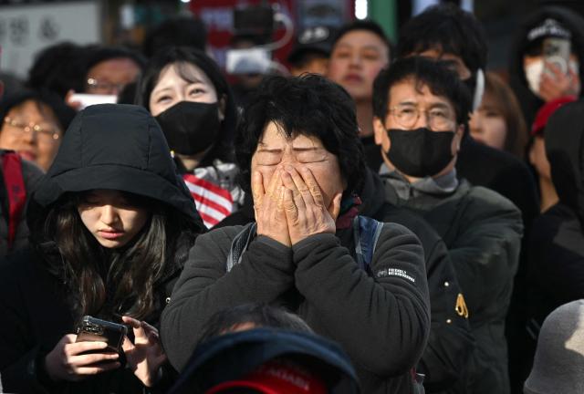 Supporters of South Korea's impeached former president Yoon Suk Yeol react as they watch a live stream of Yoon's trial on his insurrection charges near the Seoul Central District Court in Seoul on February 19, 2026. A South Korean court found ex-president Yoon Suk Yeol guilty of insurrection on February 19, and sentenced him to life in prison, saying his martial law declaration in December 2024 was a plot to "paralyse" the National Assembly. (Photo by Jung Yeon-je / AFP)