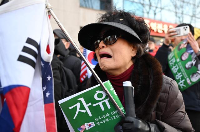 Supporters of South Korea's impeached former president Yoon Suk Yeol react as they watch a live stream of Yoon's trial on his insurrection charges near the Seoul Central District Court in Seoul on February 19, 2026. A South Korean court found ex-president Yoon Suk Yeol guilty of insurrection on February 19, and sentenced him to life in prison, saying his martial law declaration in December 2024 was a plot to "paralyse" the National Assembly. (Photo by Jung Yeon-je / AFP)