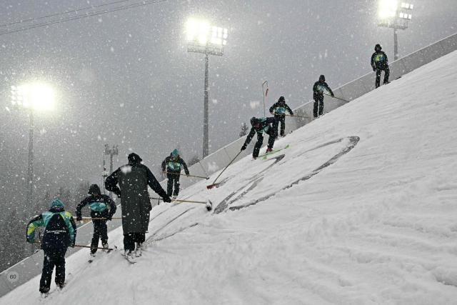 Staff groom the slope under a snowfall with brooms during the ski jumping trial round of the nordic combined team sprint large hill event at Predazzo Ski Jumping Stadium in Predazzo (Val di Fiemme) during the Milano Cortina 2026 Winter Olympic Games on February 19, 2026. (Photo by Javier SORIANO / AFP)