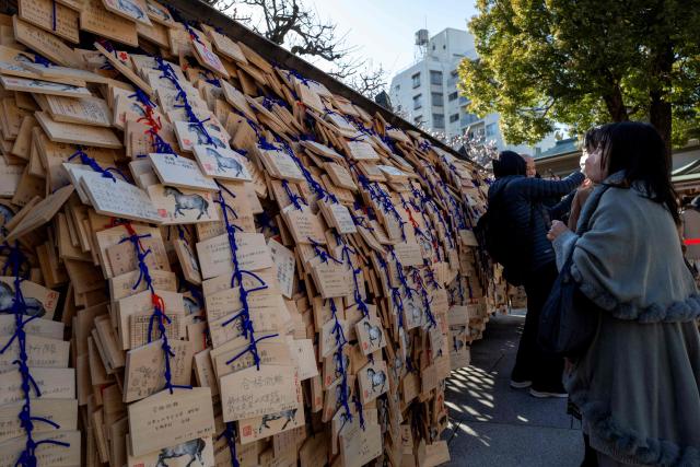 Visitors are seen beside wooden votive tablets placed by students and parents containing messages for academic success at Yushima Tenmangu Shrine in Tokyo on February 19, 2026, amid the annual entrance exam season. (Photo by Kazuhiro NOGI / AFP)