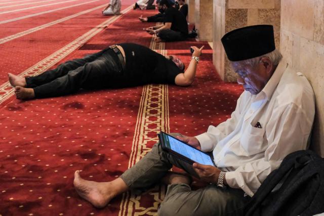 Muslim devotees read the Koran while waiting to break their fast at Istiqlal Mosque in Jakarta on February 19, 2026, during the month of Ramadan, when Muslims worldwide abstain from food, drink and sexual relations from dawn to dusk. (Photo by BAY ISMOYO / AFP)
