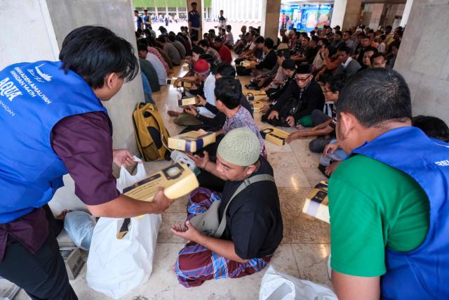 Staff members distribute iftar meals to Muslim devotees ahead of breaking their fast at Istiqlal Mosque in Jakarta on February 19, 2026, during the month of Ramadan, when Muslims worldwide abstain from food, drink and sexual relations from dawn to dusk. (Photo by BAY ISMOYO / AFP)