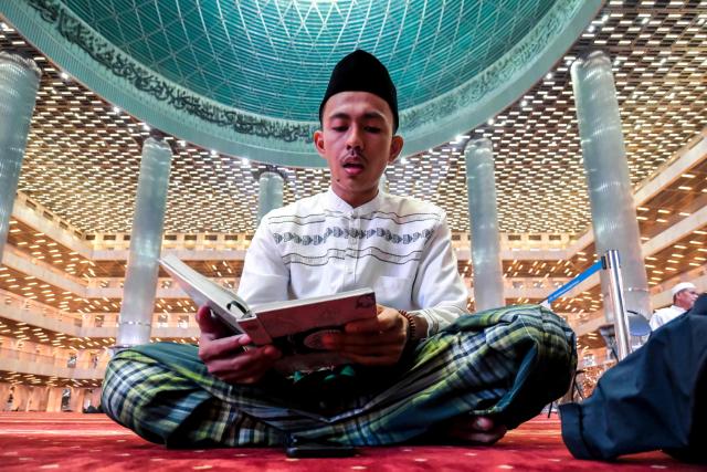 A Muslim devotee reads the Koran while waiting to break fast at Istiqlal Mosque in Jakarta on February 19, 2026, during the month of Ramadan, when Muslims worldwide abstain from food, drink and sexual relations from dawn to dusk. (Photo by BAY ISMOYO / AFP)