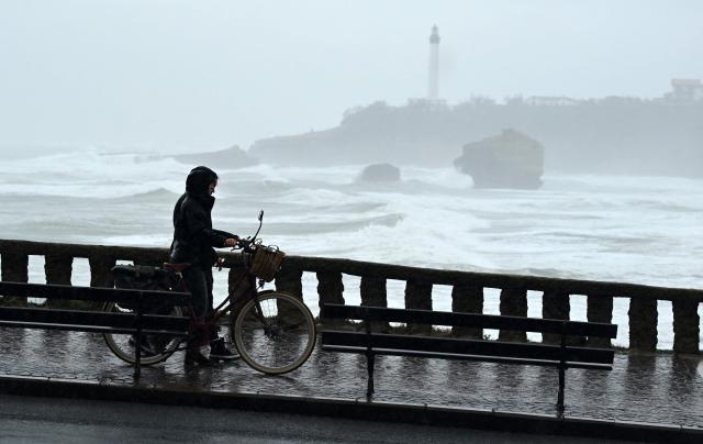 Residents walk with their bycicle near the Grande Plage, as storm Pedro hits the region, in Biarritz, south-western France on February 19, 2026. The spell of bad weather and flooding affecting France is ‘far from over’, said France’s junior Minister in charge of the environment Mathieu Lefevre on February 19, 2026. (Photo by Gaizka IROZ / AFP)
