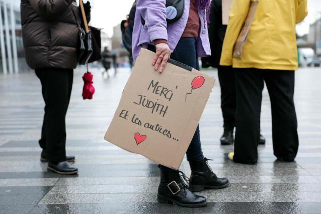 A woman holds a cardboard panel which reads as "Thank you Judith. and the other ones..." as they gather outside the Paris courthouse in support of French actress Judith Godreche in Paris on February 19, 2026. Judith Godrèche, a leading figure of #MeToo in France, has been summoned on February 19 for a procedural hearing before the Paris court, following a defamation complaint by filmmaker Jacques Doillon, whom she accuses of raping her when she was 15. (Photo by Thomas SAMSON / AFP)