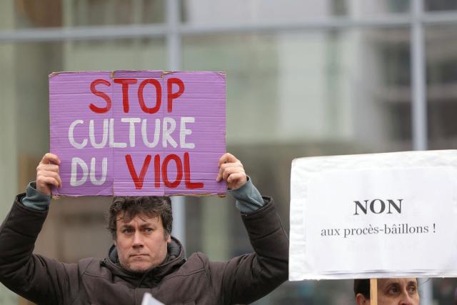 A man holds a placard which reads as "Stop rape culture" as people gather outside the Paris courthouse in support of French actress Judith Godreche in Paris on February 19, 2026. Judith Godrèche, a leading figure of #MeToo in France, has been summoned on February 19 for a procedural hearing before the Paris court, following a defamation complaint by filmmaker Jacques Doillon, whom she accuses of raping her when she was 15. (Photo by Thomas SAMSON / AFP)