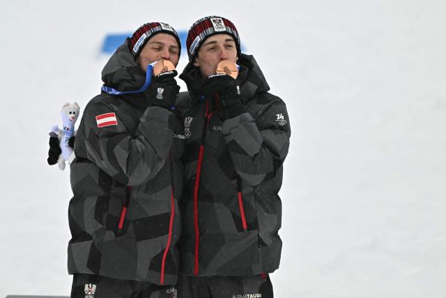 Bronze medallists Austria's Johannes Lamparter (L) and Stefan Rettenegger celebrate on the podium following the nordic combined team sprint large hill event at Tesero Cross Country Stadium at Lago di Tesero (Val di Fiemme) during the Milano Cortina 2026 Winter Olympic Games on February 19, 2026.  (Photo by Javier SORIANO / AFP)