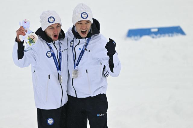 Silver medalist Finland's Ilkka Herola (L) and Finland's Eero Hirvonen celebrate on the podium following the nordic combined team sprint large hill event at Tesero Cross Country Stadium at Lago di Tesero (Val di Fiemme) during the Milano Cortina 2026 Winter Olympic Games on February 19, 2026.  (Photo by Javier SORIANO / AFP)