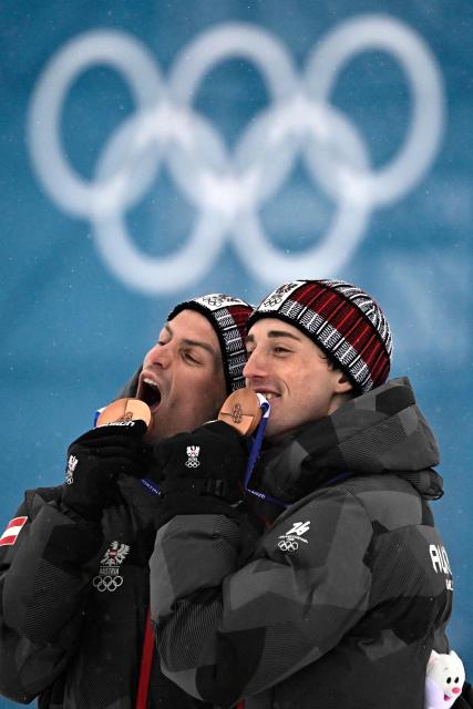 Bronze medallists Austria's Johannes Lamparter (L) and Stefan Rettenegger celebrate on the podium following the nordic combined team sprint large hill event at Tesero Cross Country Stadium at Lago di Tesero (Val di Fiemme) during the Milano Cortina 2026 Winter Olympic Games on February 19, 2026.  (Photo by Tobias SCHWARZ / AFP)