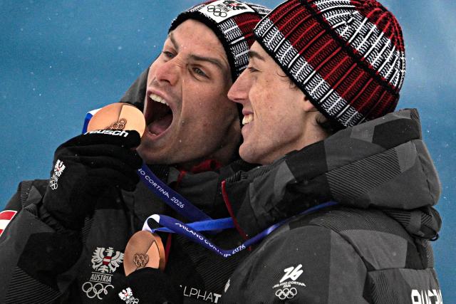 Bronze medallists Austria's Johannes Lamparter (L) and Stefan Rettenegger celebrate on the podium following the nordic combined team sprint large hill event at Tesero Cross Country Stadium at Lago di Tesero (Val di Fiemme) during the Milano Cortina 2026 Winter Olympic Games on February 19, 2026.  (Photo by Tobias SCHWARZ / AFP)